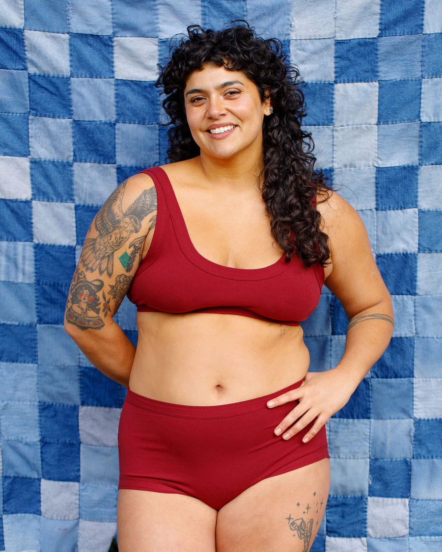 Front view studio portrait of a smiling model with tattoos posing in the Tuscan Red Thunderpants US matching underwear set.
