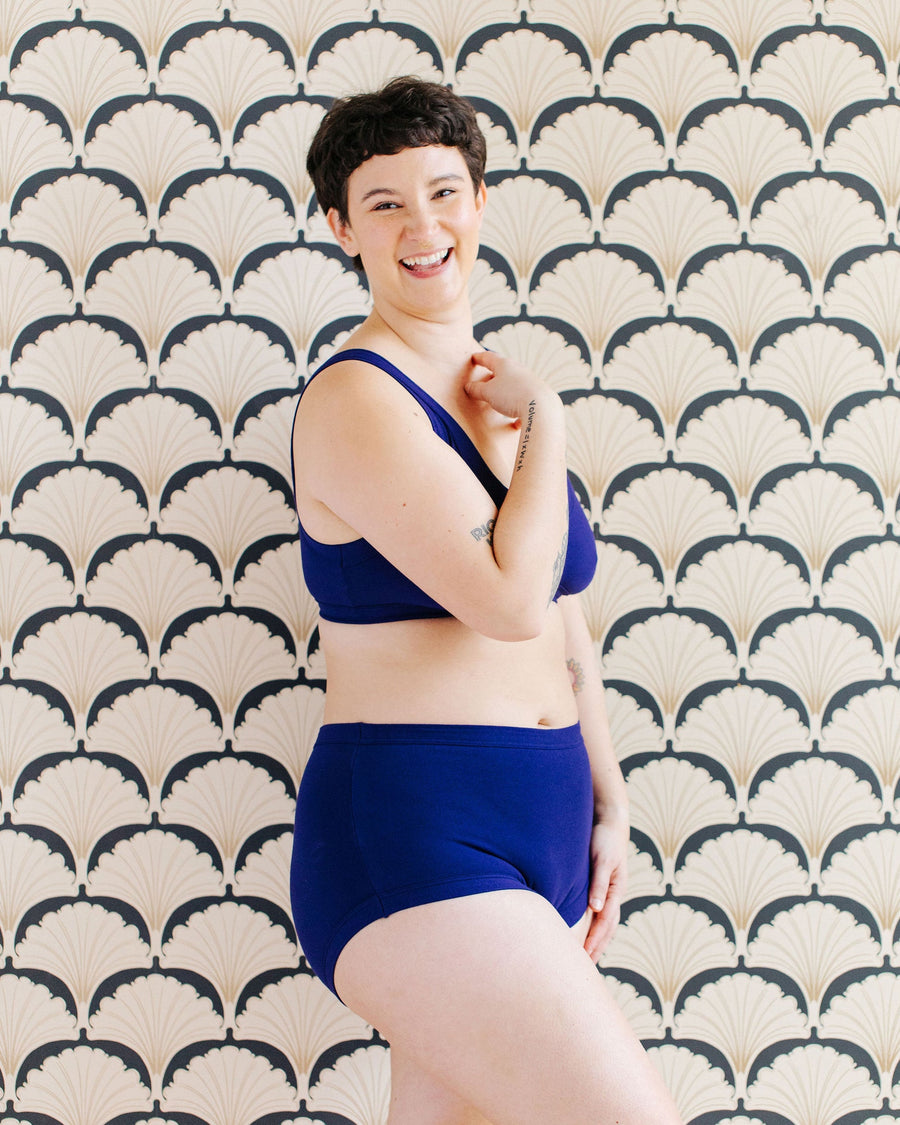 Side profile shot of a model posing in the Indigo Montoya deep blue organic cotton briefs and matching bra set.