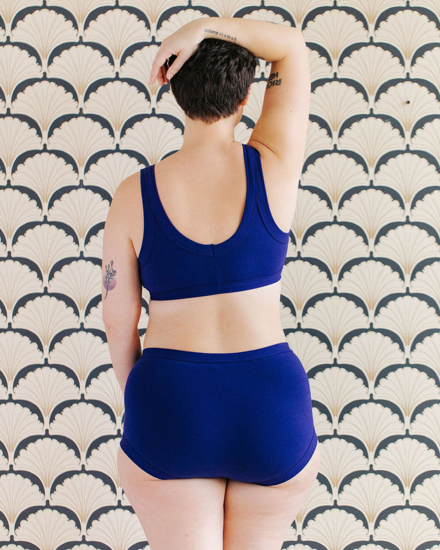 Rear view portrait showing the full back coverage fit of the Indigo Montoya deep blue organic cotton briefs.