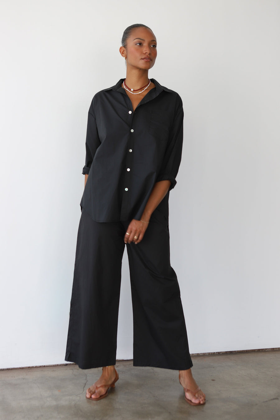 Model wearing Be Idle The Poplin Boxer Pant in black, featuring a wide-leg, relaxed fit paired with a matching button-down shirt. Shown against a plain white background.