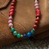 Close-up detail shot showcasing the texture and warm tones of the jade, jasper, and recycled glass beads resting on brown suede.