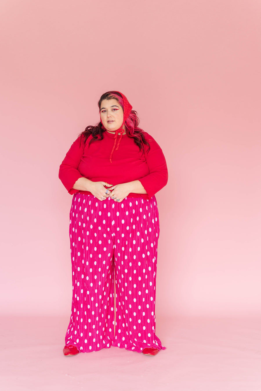Full-length front portrait of a model wearing Nettle Studios hot pink polka dot plissé wide-leg pants styled with a red top and red bonnet.
