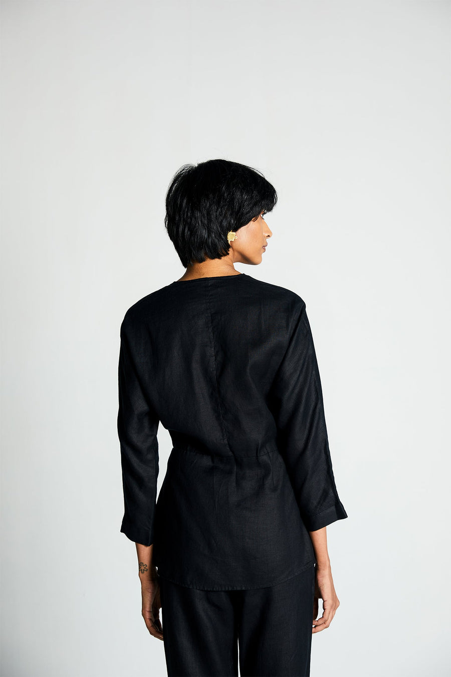 Rear profile of the 100% hemp black wrap blouse by Reistor, highlighting the clean back tailoring and cinched waist detailing. Designed for a size-inclusive collection and shown against a solid white background.