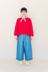 Full-length portrait of model Madison wearing the Light Floral Chambray Ruffle Pant styled with a red long-sleeve top, beanie, bandana, and yellow clogs.