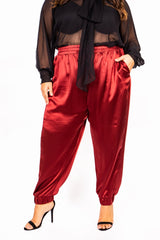 Front view of a model wearing high-waisted burgundy wine Italian silk joggers paired with a sheer black top and black heels.