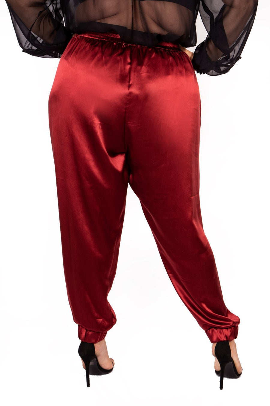 Rear view close-up of a plus-size model wearing burgundy wine high-waisted Italian silk jogger pants with elastic cuffed hems.