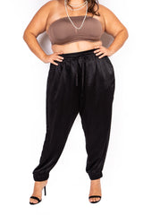 Front cropped view of a plus-size model wearing high-waisted black Italian silk jogger pants with an elastic drawstring waist and cuffed ankles.