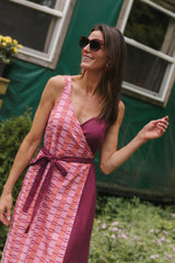 Three-quarter portrait of a model smiling outdoors in the sleeveless linen and cotton Rove wrap dress in Hibiscus.
