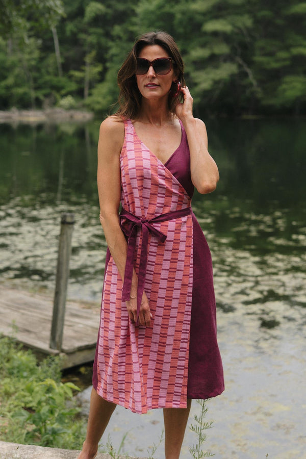 Full-length outdoor shot of a model wearing the deep V-neck Rove wrap dress in Hibiscus, featuring a pink patterned front panel tied over a deep magenta linen skirt.
