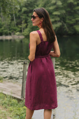 Rear view of a model by a lake showcasing the apron-style back cutout and thick straps on the magenta linen Rove Dress.