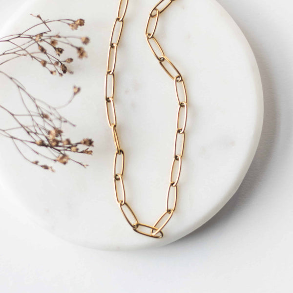 Flat lay view of the gold-plated paperclip chain Elle Necklace by Sela Designs displayed on a white marble tray with dried florals.