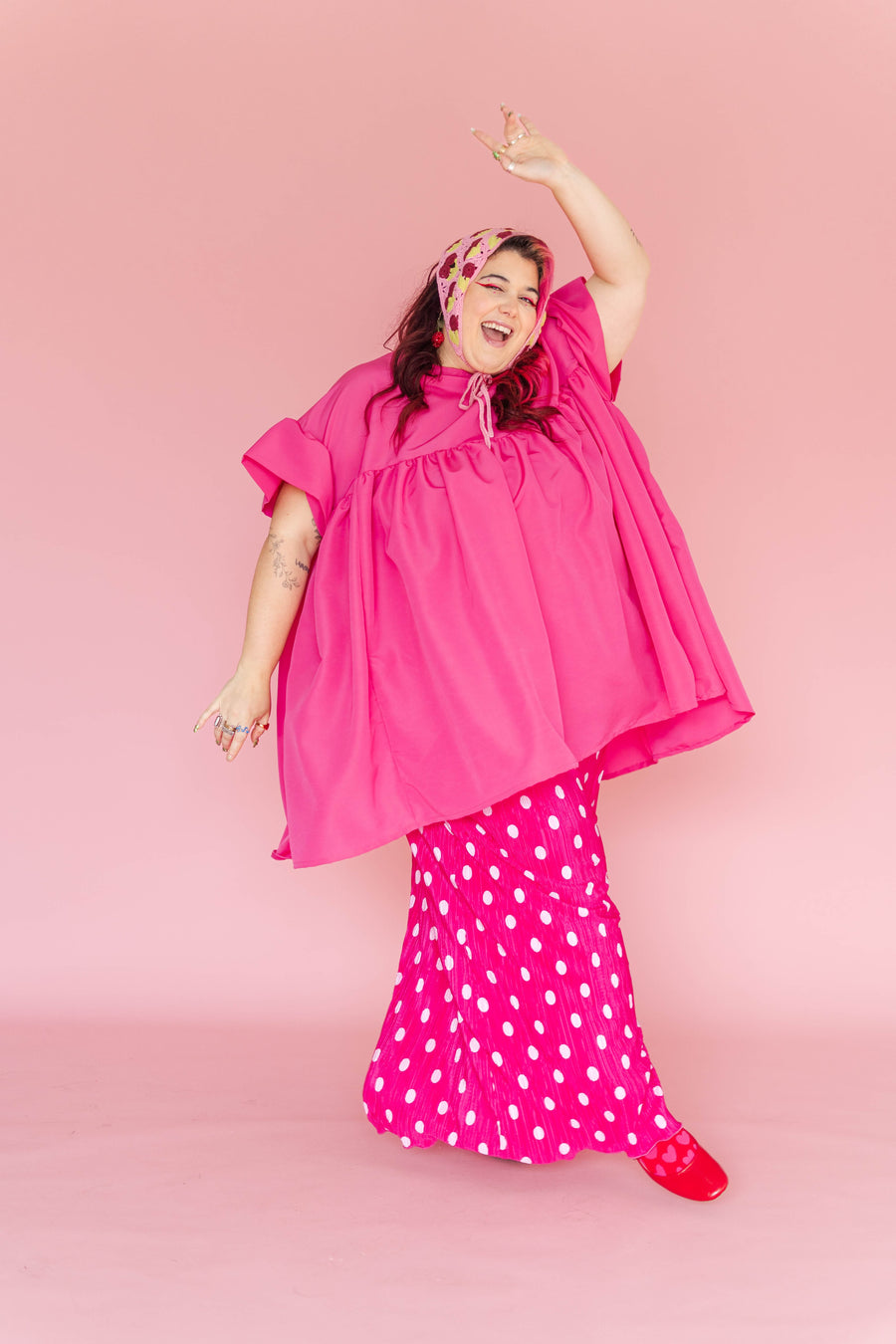Full-body shot of a model dancing while wearing the hot pink Mini Mushroom Dress layered over a pink and white polka-dot maxi skirt.