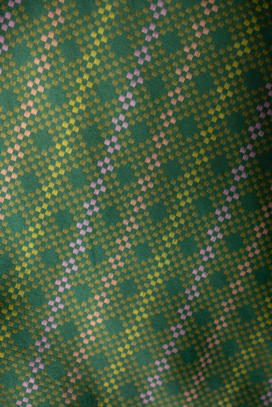 Macro fabric detail showing the woven geometric pattern and green, pink, and yellow threads on the Beth Dress in Aloe.