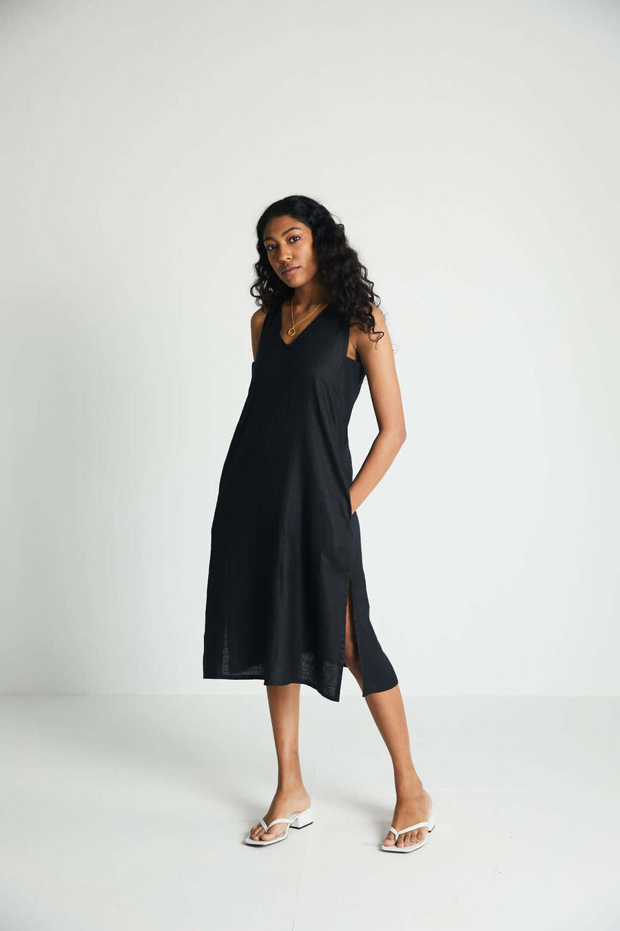 Full-body studio shot of a model standing with her hand in her pocket, highlighting the hidden side insert details and practical pocket construction of the black Hemp Noir dress.