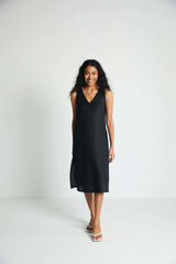A model smiling while walking forward in the sleeveless black hemp midi dress, showing off its comfortable, everyday functionality and timeless minimalist design.