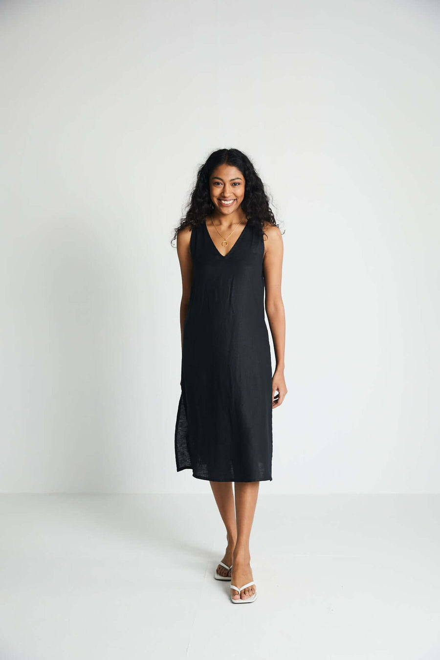 A model smiling while walking forward in the sleeveless black hemp midi dress, showing off its comfortable, everyday functionality and timeless minimalist design.