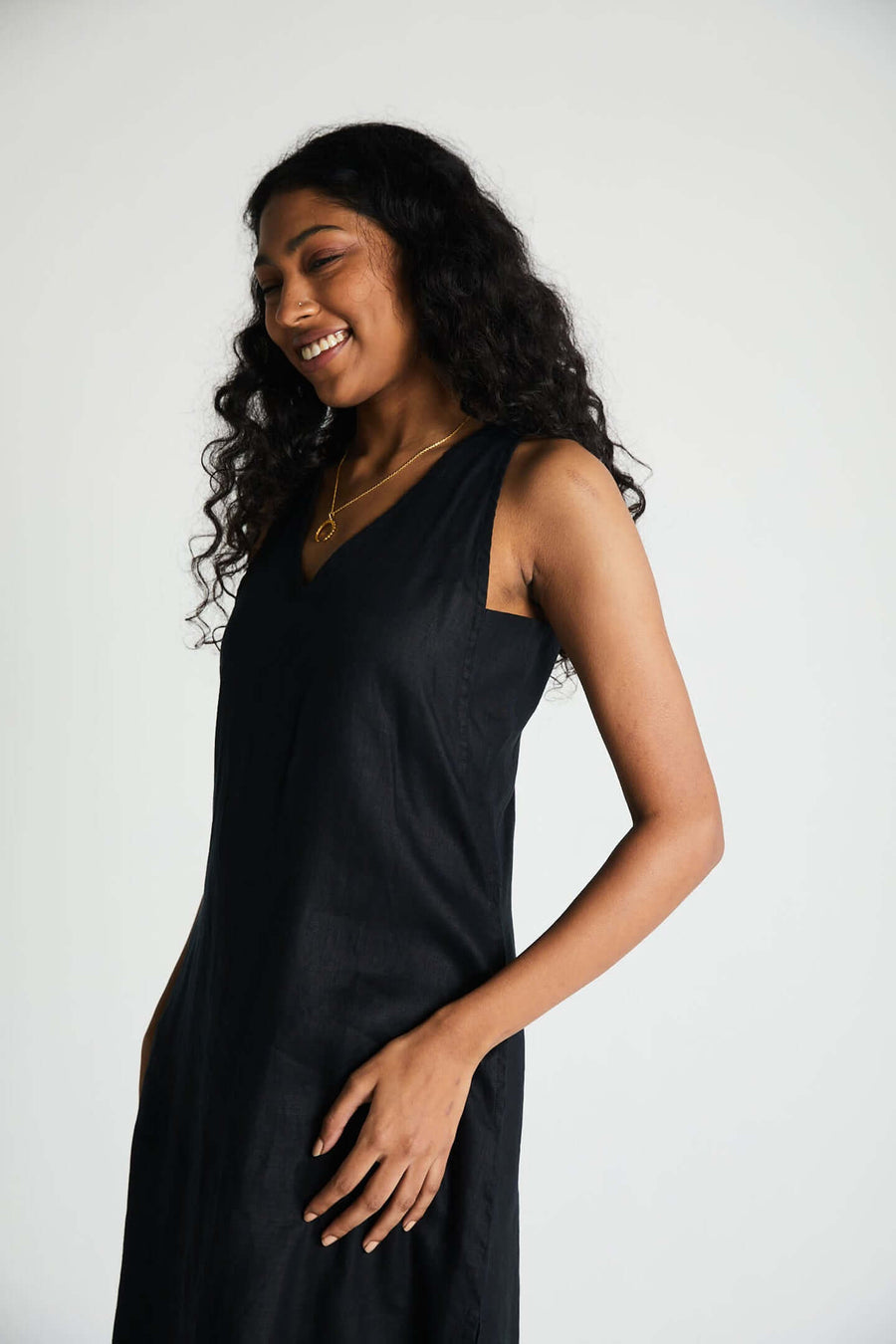 Angled medium shot of a smiling model in the black V-neck Reistor dress, emphasizing the smooth, lightweight texture of the eco-friendly textile and casual sleeveless cut.