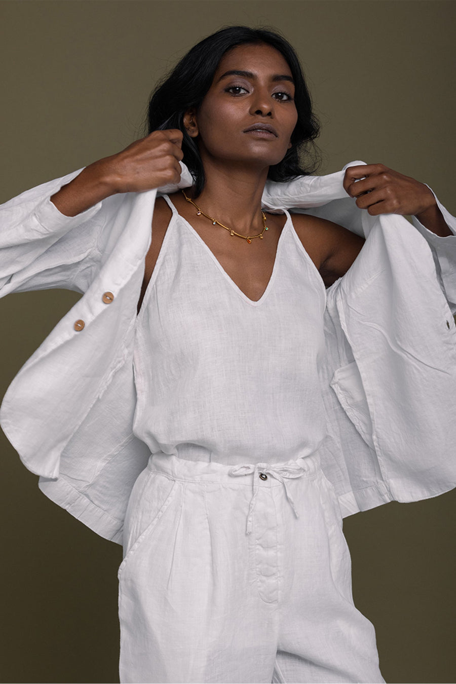 A model dynamically putting on the lightweight white hemp blazer over a matching V-neck top, displaying the flexible drape and unstructured comfort of the garment.