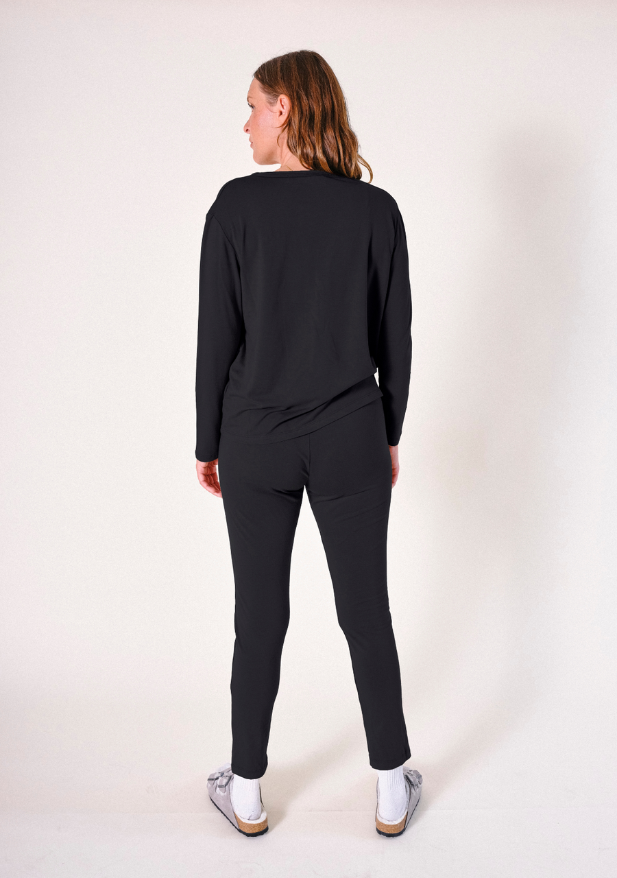 Full-length rear view of a model wearing the black Poplinen Toni PJ Pant paired with a matching long-sleeve black pajama top.