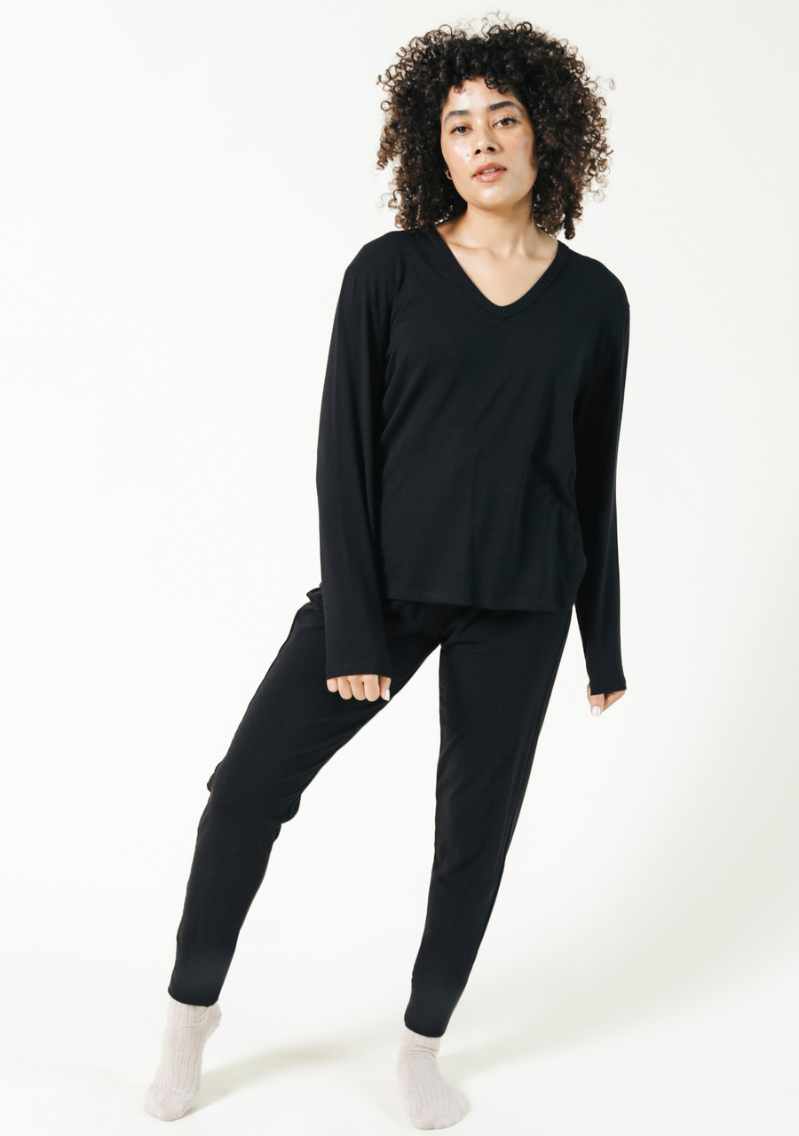 Full-body studio portrait of a model with curly hair posing in the black Poplinen Toni Pajama set with a V-neck top and tapered lounge pants.
