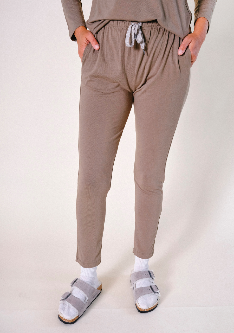 Front cropped shot of a model wearing olive-brown Poplinen Toni Pajama Pants with hands in pockets and a grey drawstring waist.