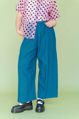 Mid-section close-up highlighting the elastic waist, side pockets, and wide-leg cut of the teal linen pants styled with a sheer polka-dot shirt.