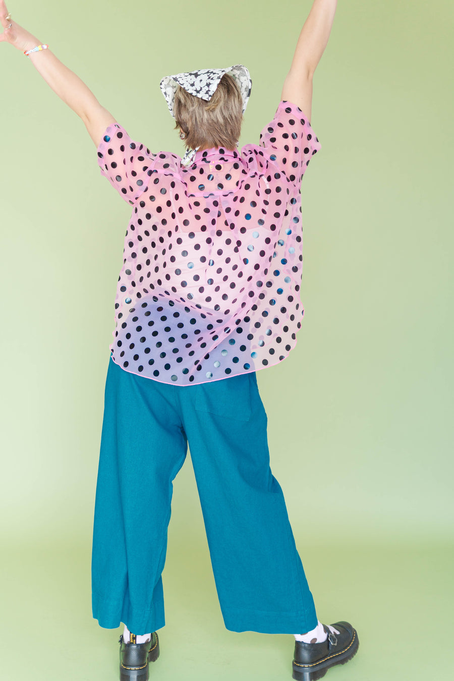 Back view of model celebrating with arms raised, showing the lightweight sheer pink polka dot fabric and relaxed hemline.