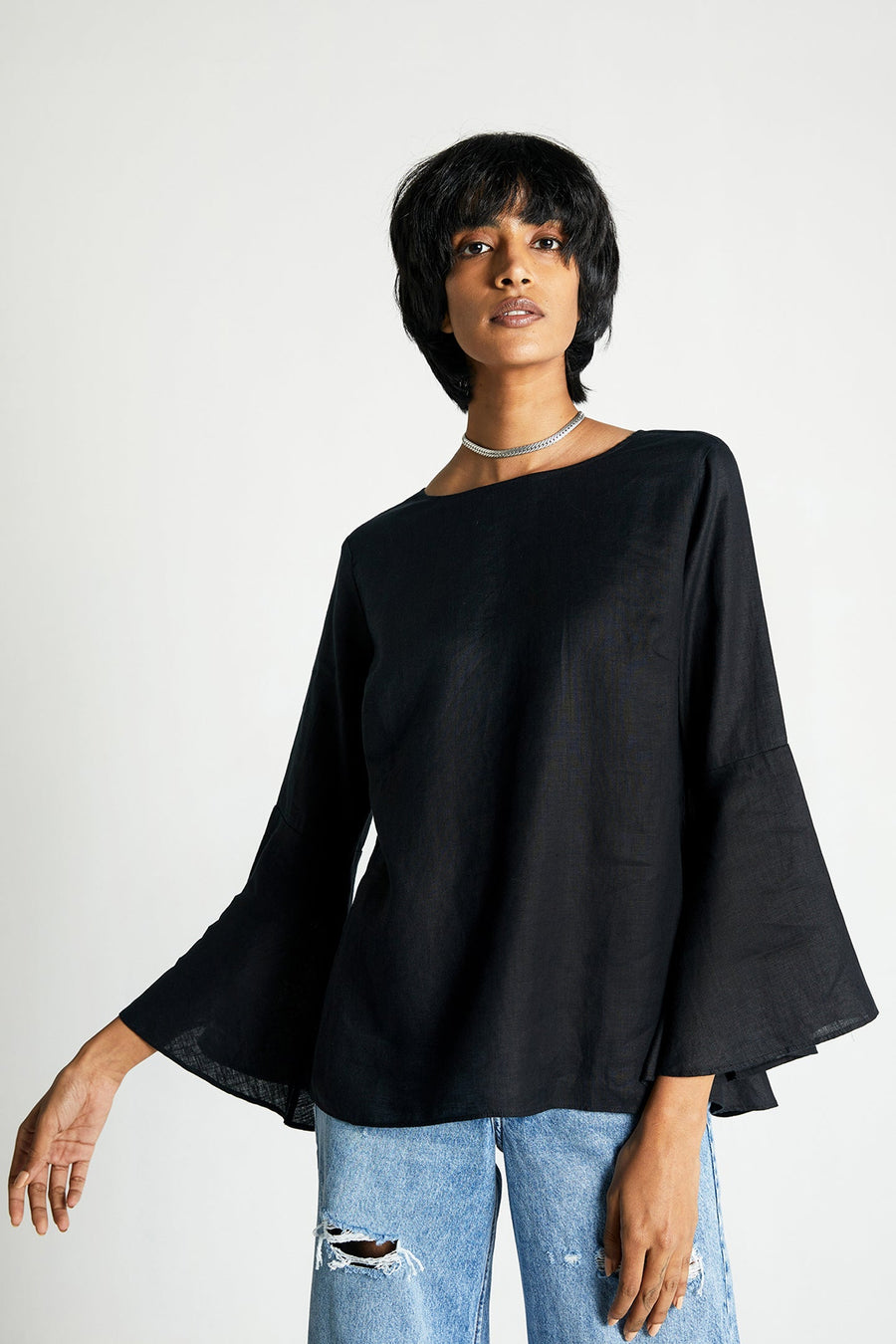 Front view of a straight-size model presenting the black hemp boat-neck blouse, emphasizing its timeless regular-fit silhouette paired with high-waisted distressed denim.