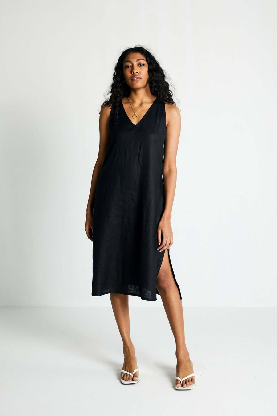 Full-length front view of a model presenting the minimalist black Hemp Noir dress, showcasing its easy, edgy cut and loose silhouette styled with casual white thong sandals.