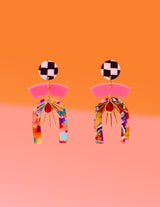 Tribe and Temple Confetti Multi Mixed Media Earrings featuring a black and white checkered stud, pink arc, and a multicolored confetti resin arch with a gold-plated sunburst and red teardrop center on an orange and pink background.