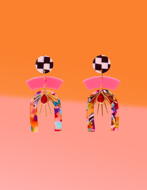 Tribe and Temple Confetti Multi Mixed Media Earrings featuring a black and white checkered stud, pink arc, and a multicolored confetti resin arch with a gold-plated sunburst and red teardrop center on an orange and pink background.