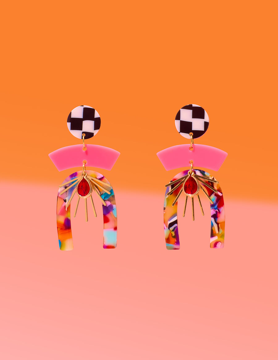 Tribe and Temple Confetti Multi Mixed Media Earrings featuring a black and white checkered stud, pink arc, and a multicolored confetti resin arch with a gold-plated sunburst and red teardrop center on an orange and pink background.