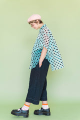 Side profile view of a model walking, showcasing the dramatic flared drape and unique curved petal silhouette of the Nettle Studios Sheer Mint Chocolate Chip Polka Dot Tulip Top in a size-inclusive fit.