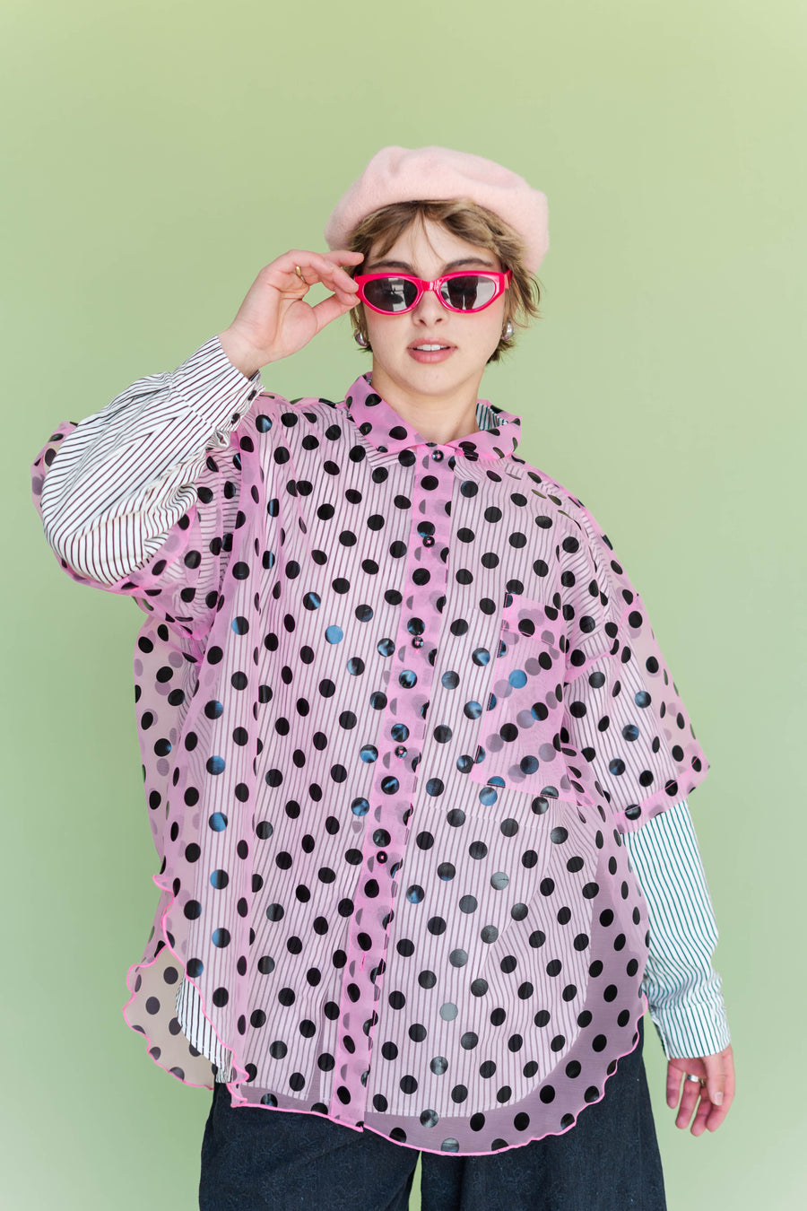 Front view of model wearing Nettle Studios sheer pink polka dot button-up layered over a striped long-sleeve shirt with a pink beret.