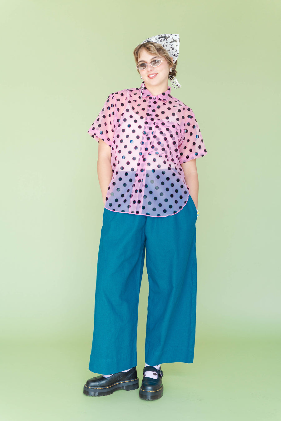 Full-body front view of a model wearing teal wide-leg linen pants with hands in pockets against a light green background.