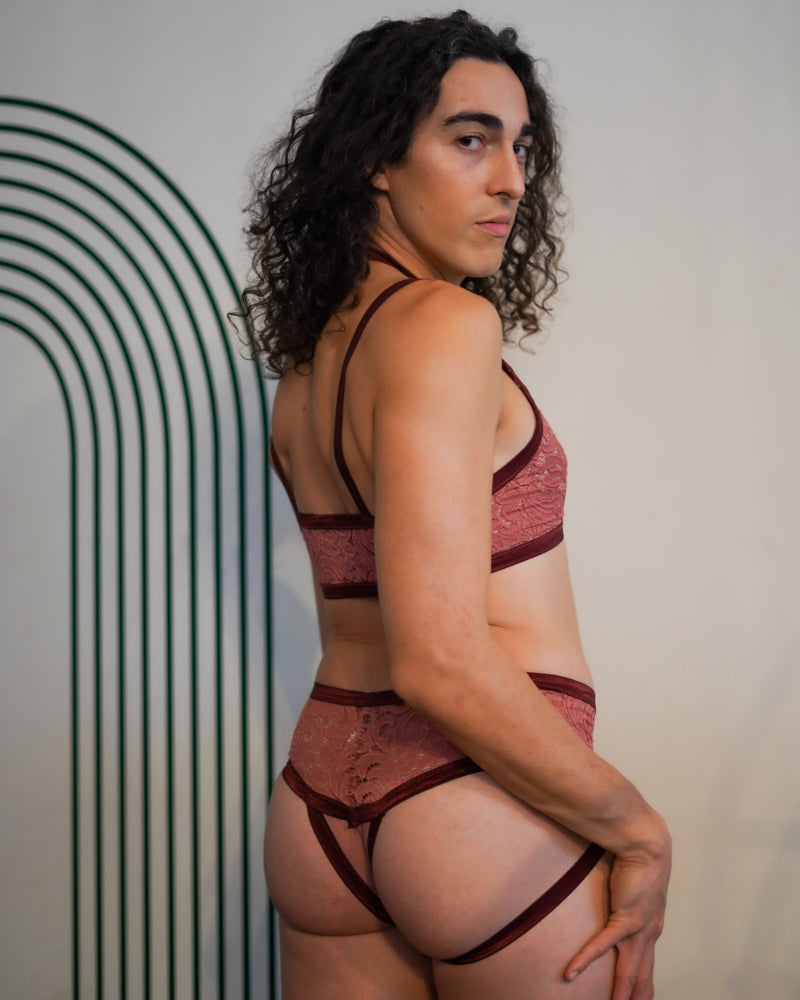 Side rear view of a model with dark curly hair wearing plum-colored lace cantiqLA Bandage Briefs with satin elastic straps.