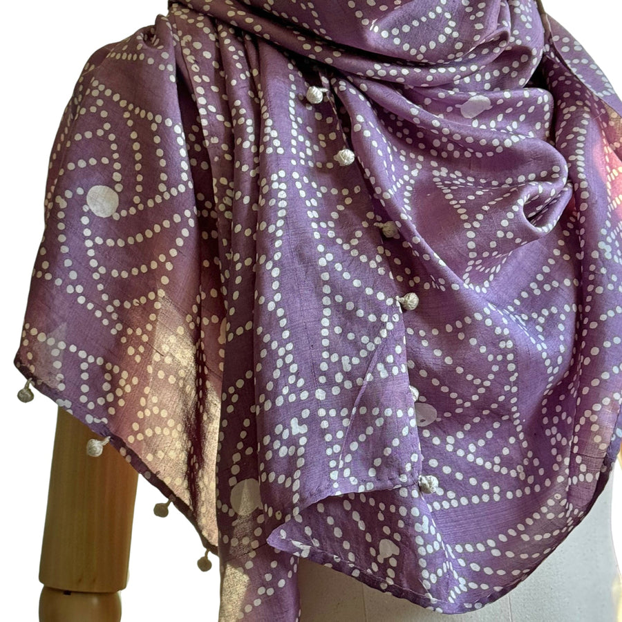 Close-up view of the DEWBERRY Batik Hand Block Printed Scarf arranged over a wooden mannequin torso, illustrating the distinct sheen of the premium handwoven Malda silk and the detailed rows of white hand-knotted round tassels.