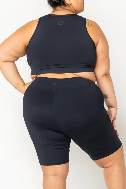 Rear close-up view of a plus-size model wearing high-waisted black 9-inch swim shorts and a matching black swim top.