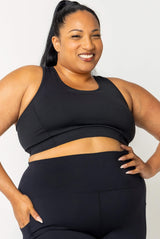 Front view close-up of a smiling plus-size model wearing the black SuperHold Racerback Sports Bra with matching high-waisted leggings.