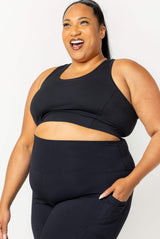 Three-quarter front view of a model wearing the black SuperHold racerback sports bra paired with black pocket leggings.