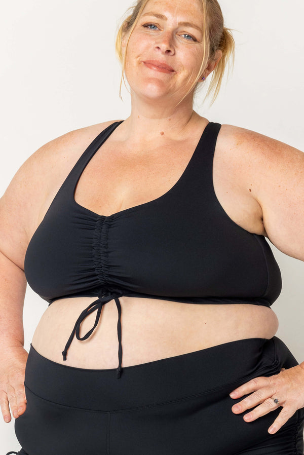Front view close-up of a blonde plus-size model wearing the black Superfit Hero Cinched Bikini Swim Top with an adjustable front drawstring.