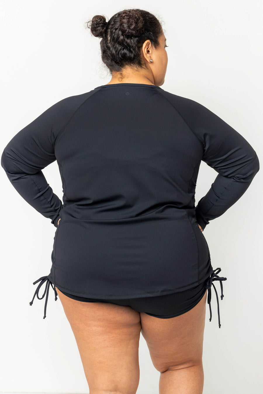 Rear view of a model wearing the black long sleeve UV swim rash guard, demonstrating full back coverage and side drawstrings.
