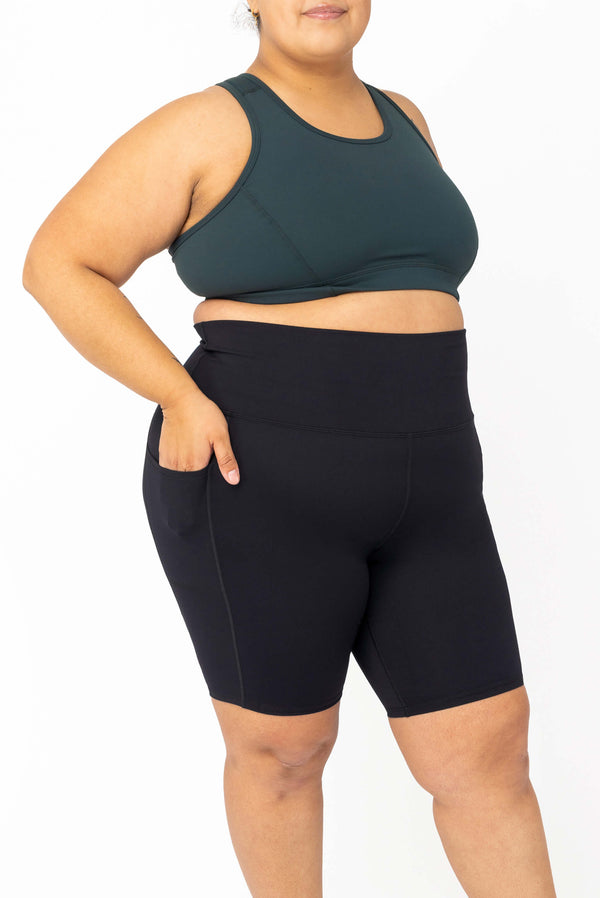 Front-three-quarter view of a model placing her hand inside the side pocket of the black SuperHold 9-inch bike shorts by Superfit Hero.