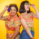 Studio photoshoot against a yellow backdrop featuring the Blue Platypus Brownstone Betties Jumpsuit styled with a wide mustard belt.
