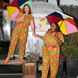 Full-length view of two models holding open rainbow umbrellas while wearing the retro graphic printed Blue Platypus Brownstone Betties Jumpsuit.