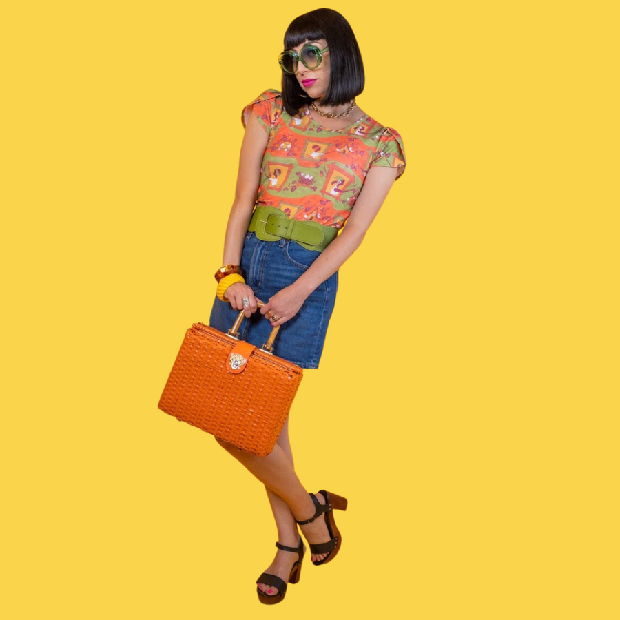 Model posing with hand on hip wearing the Blue Platypus Brownstone Betties Tulip Sleeve Tee paired with a green belt and denim skirt.