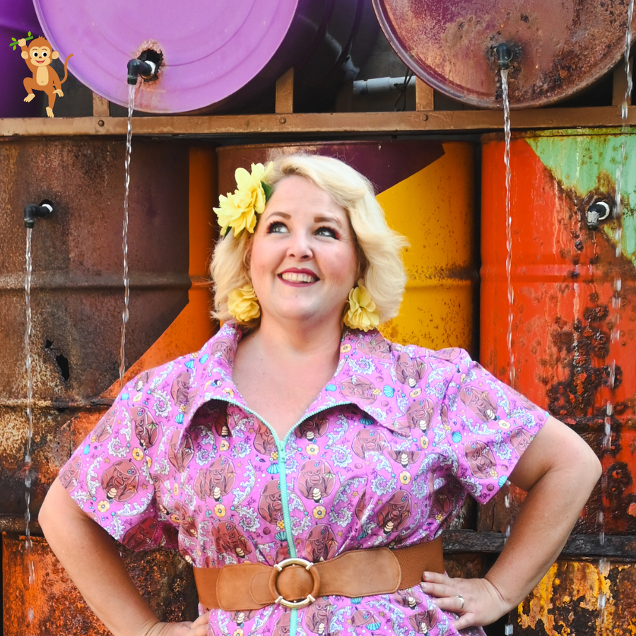 Studio portrait of a blonde model with a yellow flower in her hair wearing the Blue Platypus Cheeky Tiki Monkeys Jumpsuit in Magenta.