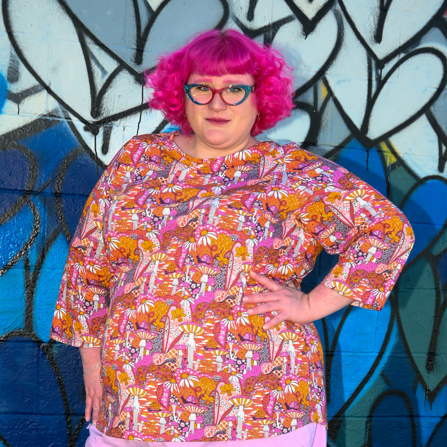 Medium shot of model posing with hand on hip in the vibrant orange and pink mushroom printed Blue Platypus 3/4 sleeve tee.