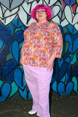 Model with pink curly hair posing in front of a graffiti heart wall wearing the Blue Platypus Groovy Mushroom 3/4 Sleeve Tee in Sunset.