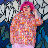 Model with pink curly hair posing in front of a graffiti heart wall wearing the Blue Platypus Groovy Mushroom 3/4 Sleeve Tee in Sunset.